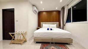 A hotel room with a bed, a wooden headboard, a window with curtains, a wall-mounted air conditioner, and a small wooden drying rack. - Patong Beachfront Superior Room (Tambon Patong)
