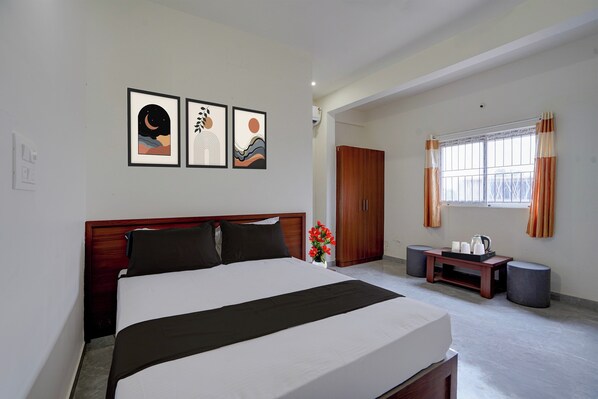 Hotelkamer met een bed, nachtkastje met een bloevas, raam met gordijnen en een kunstwerk aan de muur.