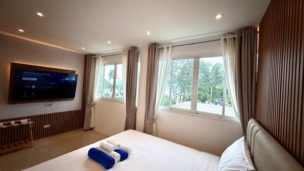 A hotel room with a bed, a television mounted on the wall, and a window with curtains.