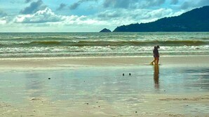 A beach with waves, a person walking, and distant mountains.