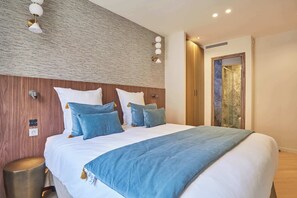 A hotel room with a large bed, a wooden headboard, a textured wall, a small bedside table, and a bathroom with a glass door. - Elegant Apartment AC St Germain Luxembourg Park (Paris)
