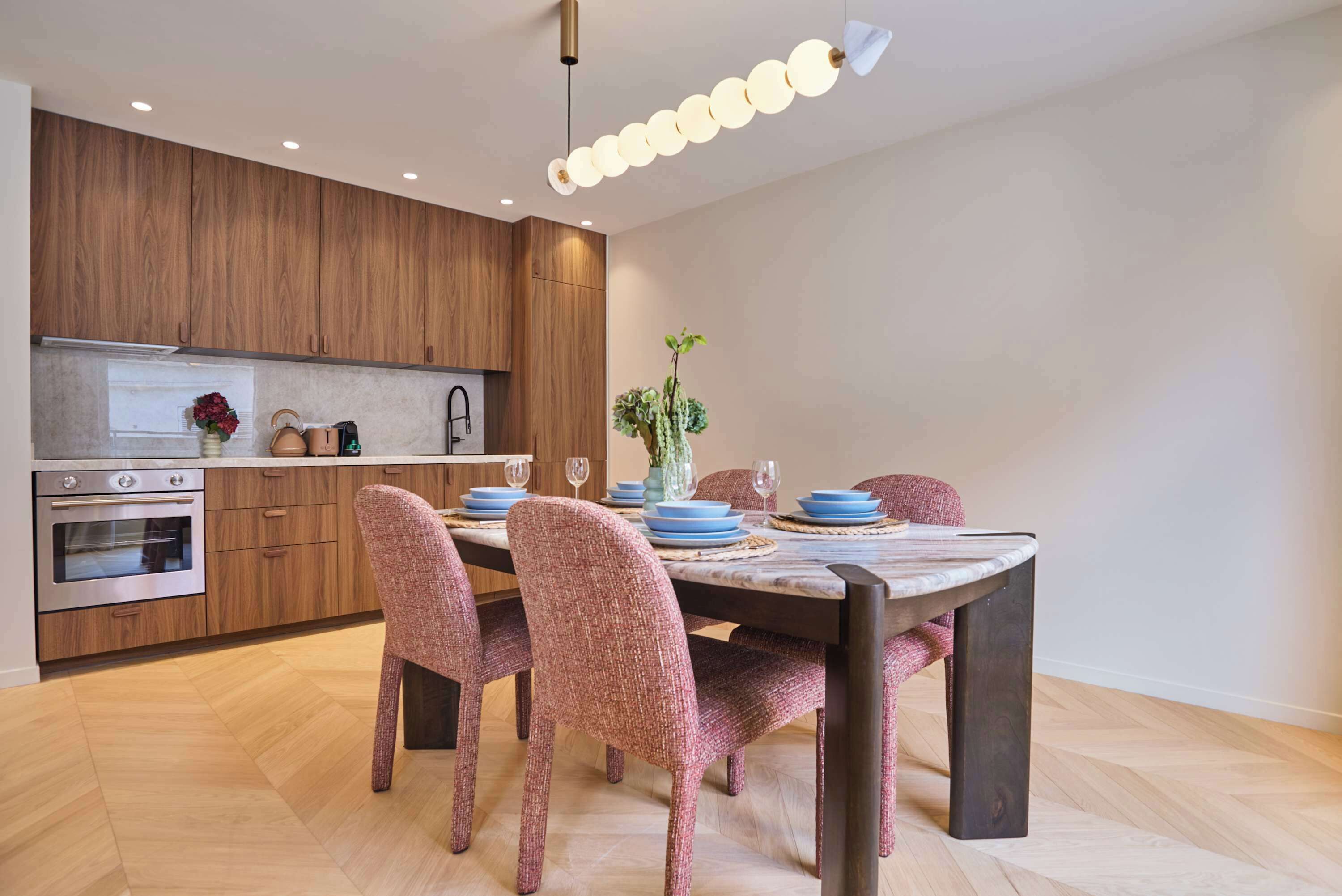 Une cuisine moderne avec des meubles en bois, des appareils en acier inoxydable et un coin repas comprenant une table en marbre et des chaises à motifs.