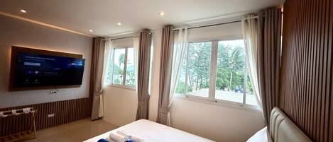 Una habitación de hotel con una cama, televisión montada en la pared y una ventana con cortinas.