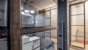 Een kamer met een grote spiegel, een radiator en een raam met jaloezieën.