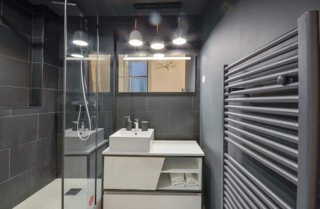 Un baño moderno con cabina de ducha de vidrio, un lavamanos blanco con espejo encima y un perchero en la pared.