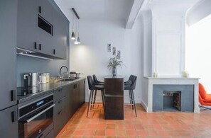A modern kitchen with dark cabinetry, a central island, and a dining area with a fireplace. - Elegant, air-conditioned apartment in the heart of Aix • 2 minutes from City Hall (Aix-en-Provence)