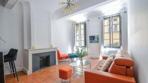 Een woonkamer met een open haard, een oranje bank en twee fauteuils.