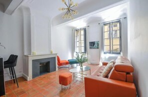 A living room with a fireplace, orange sofa, and two chairs. - Elegant, air-conditioned apartment in the heart of Aix • 2 minutes from City Hall (Aix-en-Provence)
