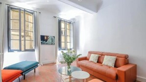 Een kamer met een bank, een klein tafeltje, een bankje en een raam met gordijnen.