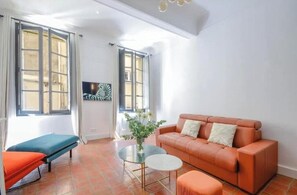 A room with a sofa, a small table, a bench, and a window with curtains. - Elegant, air-conditioned apartment in the heart of Aix • 2 minutes from City Hall (Aix-en-Provence)
