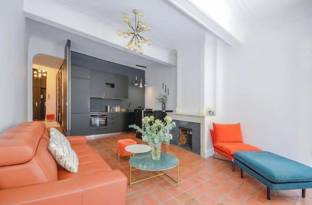 A modern living room with a sofa, ottoman, and a small table with a vase.