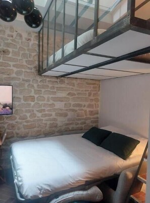 A bedroom with a stone wall, a bed with pillows, a glass railing, and a staircase. - The Little Workshop of Light • Air Conditioning & Sunrooms in the Heart of Paris (Île-de-France)