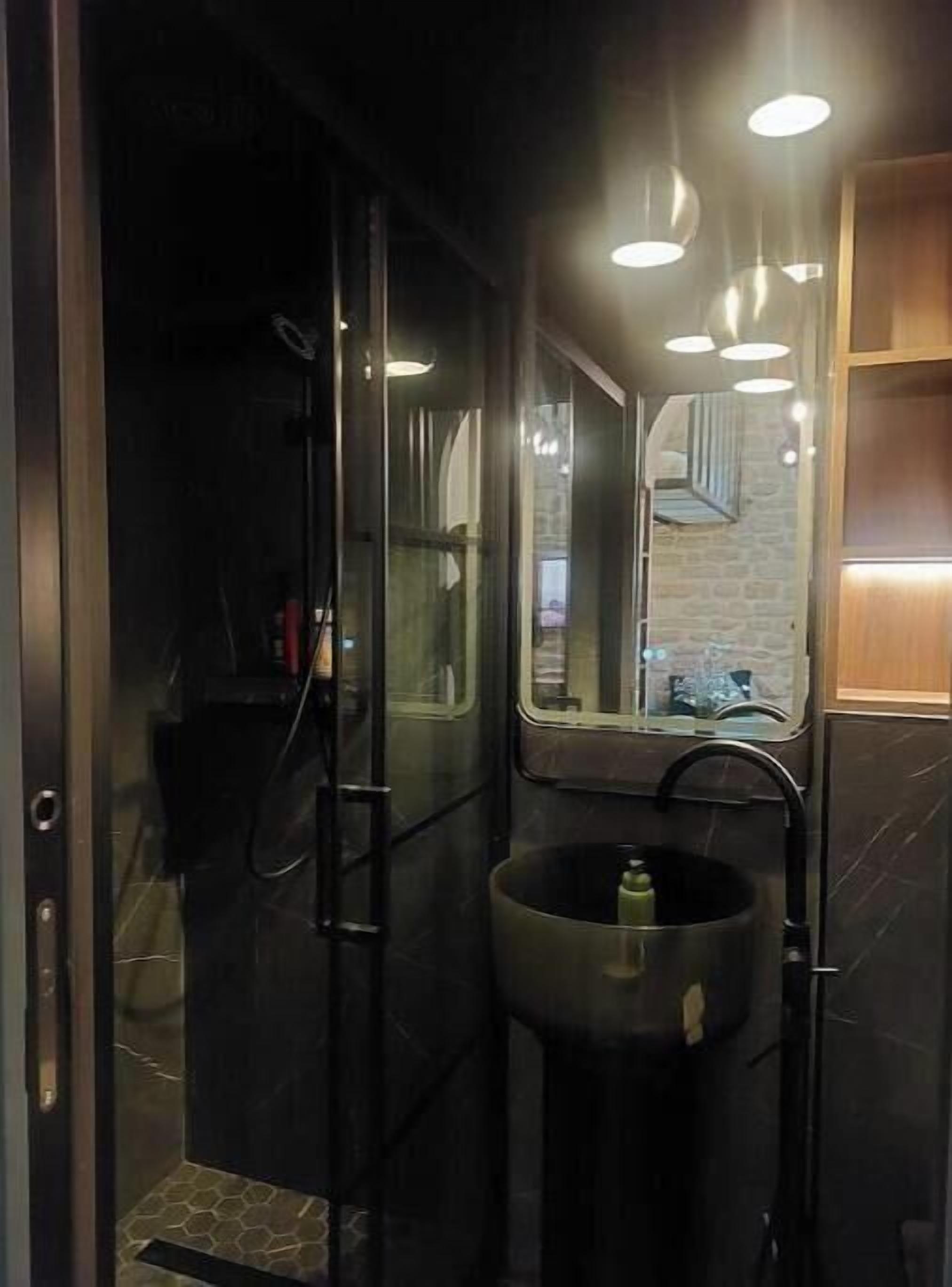 Un baño moderno con cabina de ducha de vidrio, un lavabo grande y un espejo que refleja el ambiente.