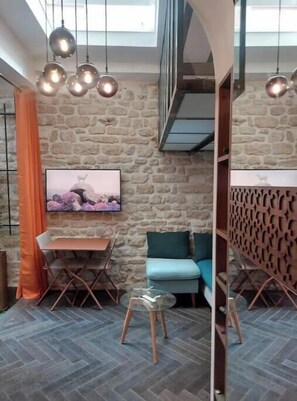 A room with a stone wall, a television, a sofa, a table, and a chair. - The Little Workshop of Light • Air Conditioning & Sunrooms in the Heart of Paris (Île-de-France)