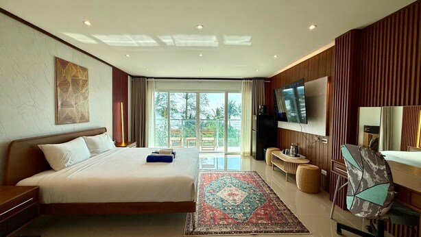 A hotel room with a large bed, a TV, a desk, and a view of the outdoors. - Deluxe Beachfront Room, Balcony & Sea View (Tambon Patong)