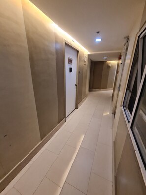 A hotel corridor with a tiled floor, a door with a sign, and a window on the right.