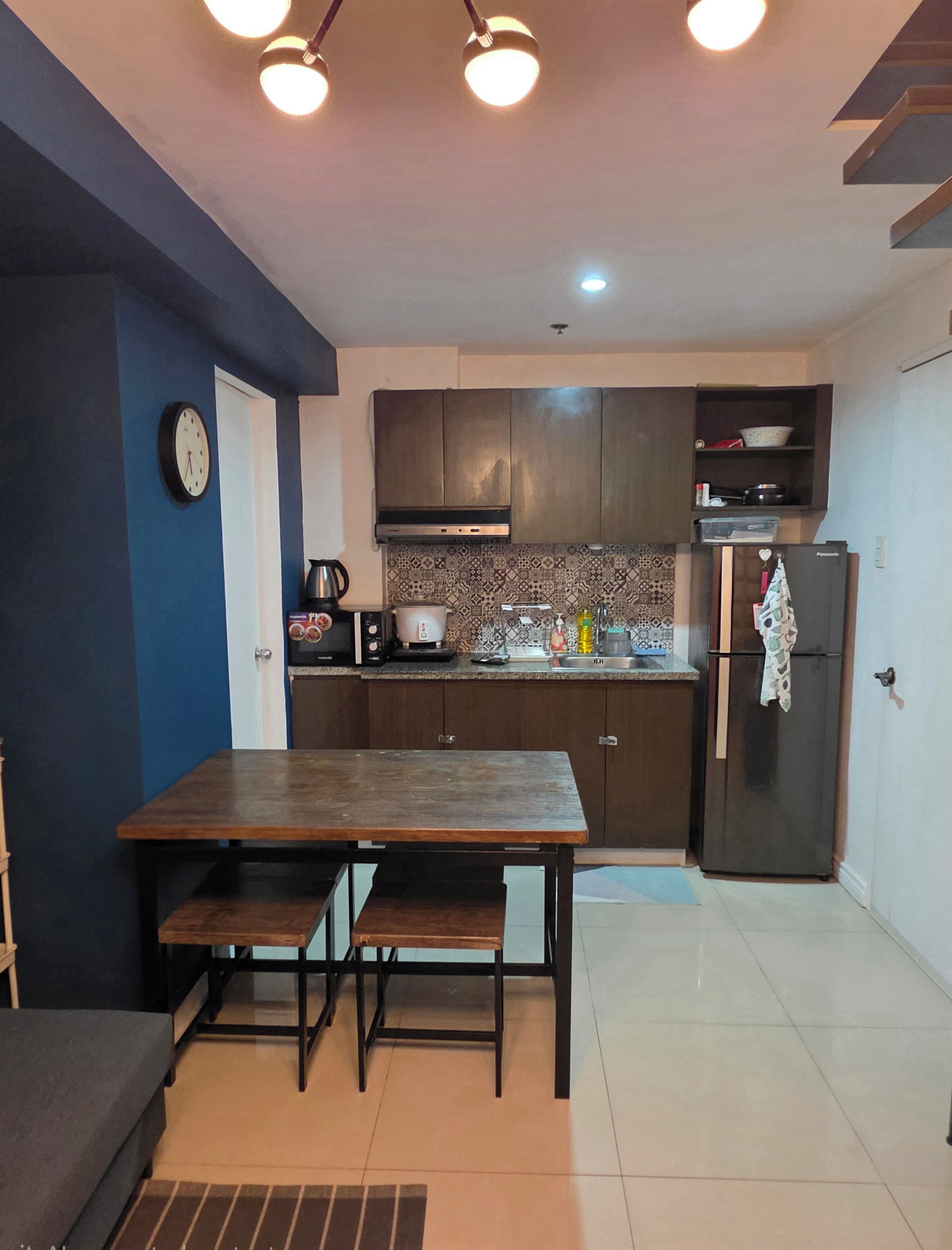 A compact kitchen with a wooden table, dark cabinets, and a refrigerator.