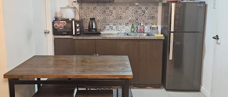 Una cocina compacta con una mesa de madera, asientos tipo banca, un refrigerador y un microondas.