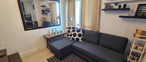 A modern living room with a grey sofa, a small side table, a mirror, and a black and white patterned pillow.