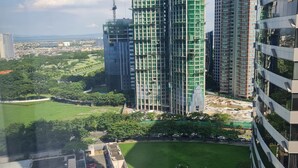 A high-rise building with a construction crane, surrounded by greenery and other buildings.