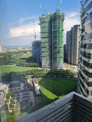 A high-rise building with a construction crane, surrounded by greenery and other buildings.