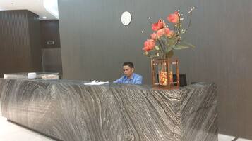 A reception desk with a marble top, a clock on the wall, and a vase with flowers.