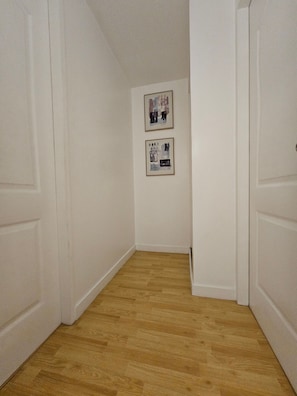A narrow hallway with wooden flooring and white walls. There are two framed pictures on the wall. - Casa Rosa1 2BR in BGC 5th Ave Wifi 300 Mbps 5 pax (Taguig)