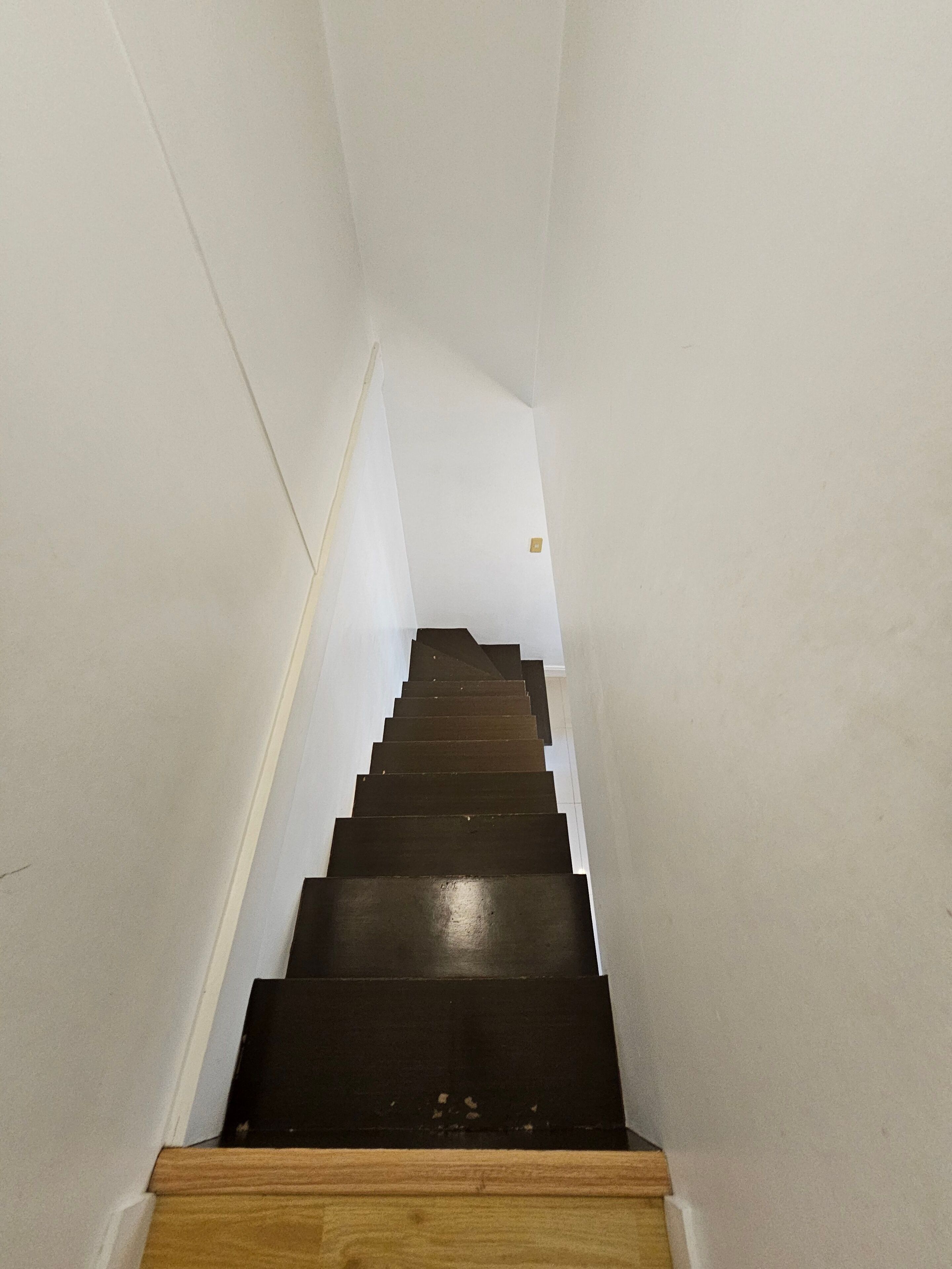 A narrow staircase with wooden steps and white walls.