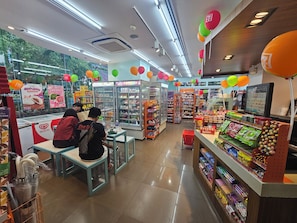 A brightly lit convenience store with refrigerated sections, shelves stocked with snacks, and a checkout area. - Casa Rosa1 2BR in BGC 5th Ave Wifi 300 Mbps 5 pax (Taguig)
