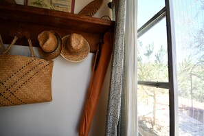 Una habitación con ventana, un estante de madera con sombreros y un bolso tejido, y una cortina estampada.