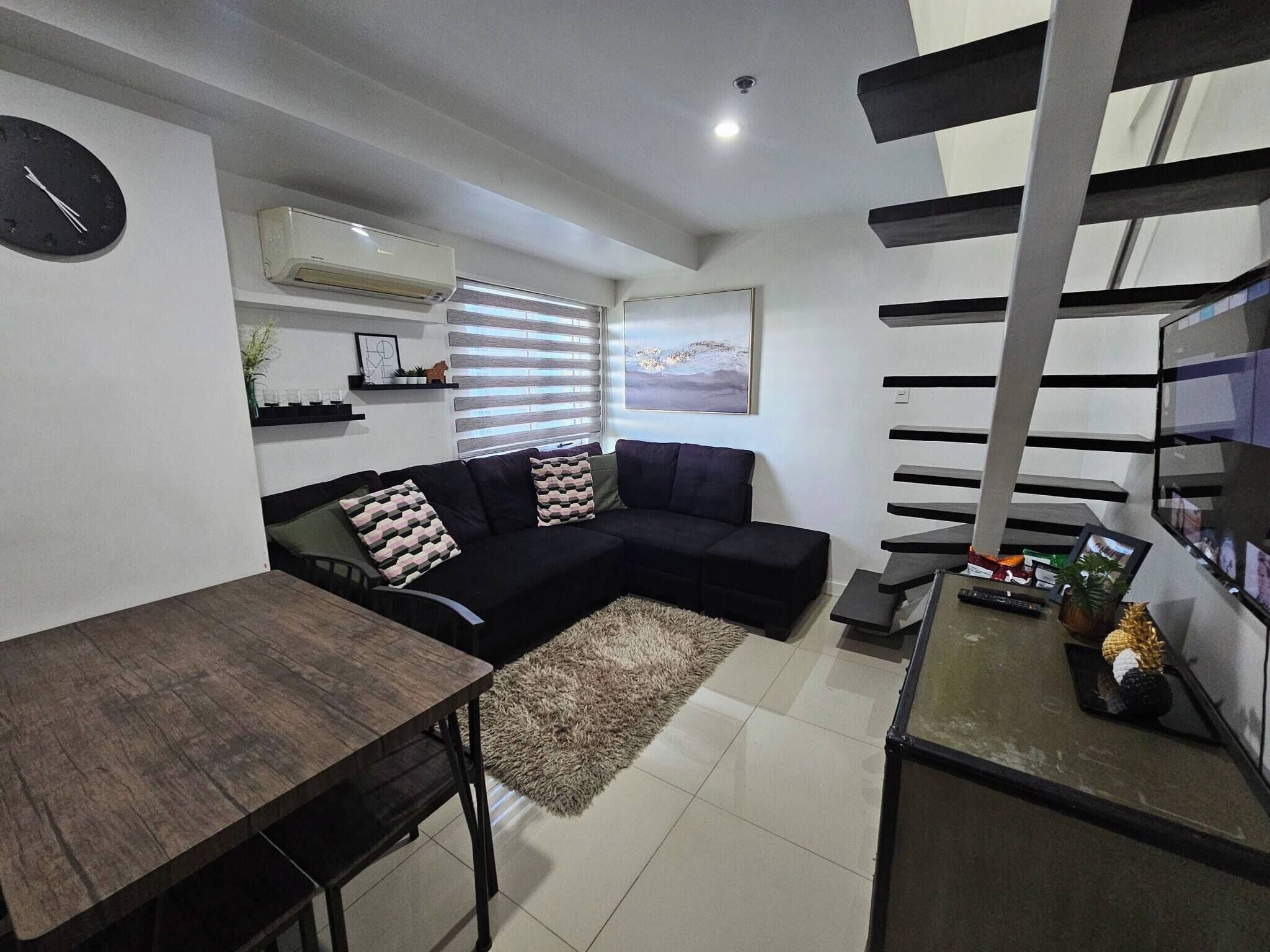 Una sala moderna con un sofá modular, una mesa de comedor y una escalera.