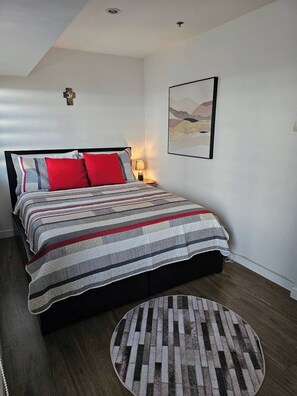 A bedroom with a bed, a round rug, a nightstand, a lamp, and a wall art piece. - Casa Rosa3 2BR Loft in BGC 5 People (Taguig)