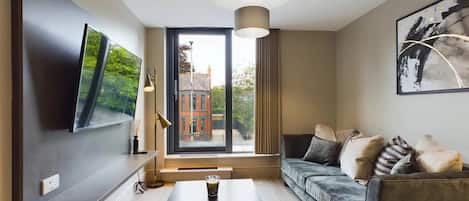 A modern living room with a sofa, a coffee table, and a large window offering a view of buildings and trees.