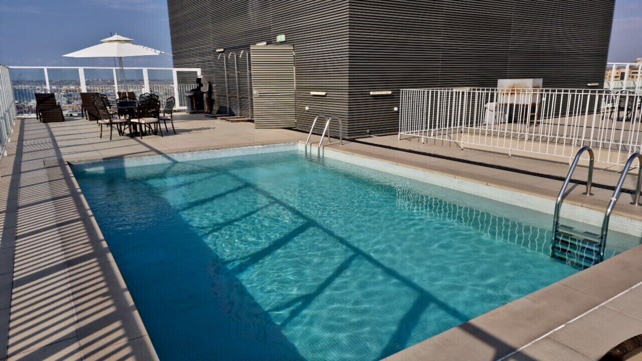 En pool på taget med udsigt over byen, et overdækket opholdsområde og et metalhegn.