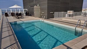 Una piscina al terrat amb vista a la ciutat, una zona de seients coberta i una tanca metàl·lica.