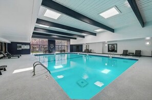 Ein großer, überdachter Pool mit klarem Wasser, umgeben von Liegestühlen und einer Decke mit Dachfenstern.