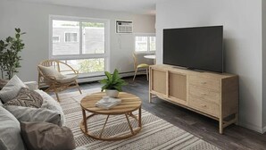 A living room with a sofa, a round coffee table, a TV on a wooden cabinet, and a large window with blinds. - Cozy MSP 1BR Retreat: Pets OK, Pool & Gym-159/nt, 4499/mn{Negotiable} (Minneapolis)
