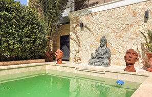 A pool area with a Buddha statue and a child statue, surrounded by greenery and a stone wall. - EL ARENAL - CALA ESTANCIA N6 (Mallorca)