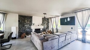 Uma sala de estar moderna com uma parede de pedra, lareira, sofá grande e televisão de tela plana na parede.