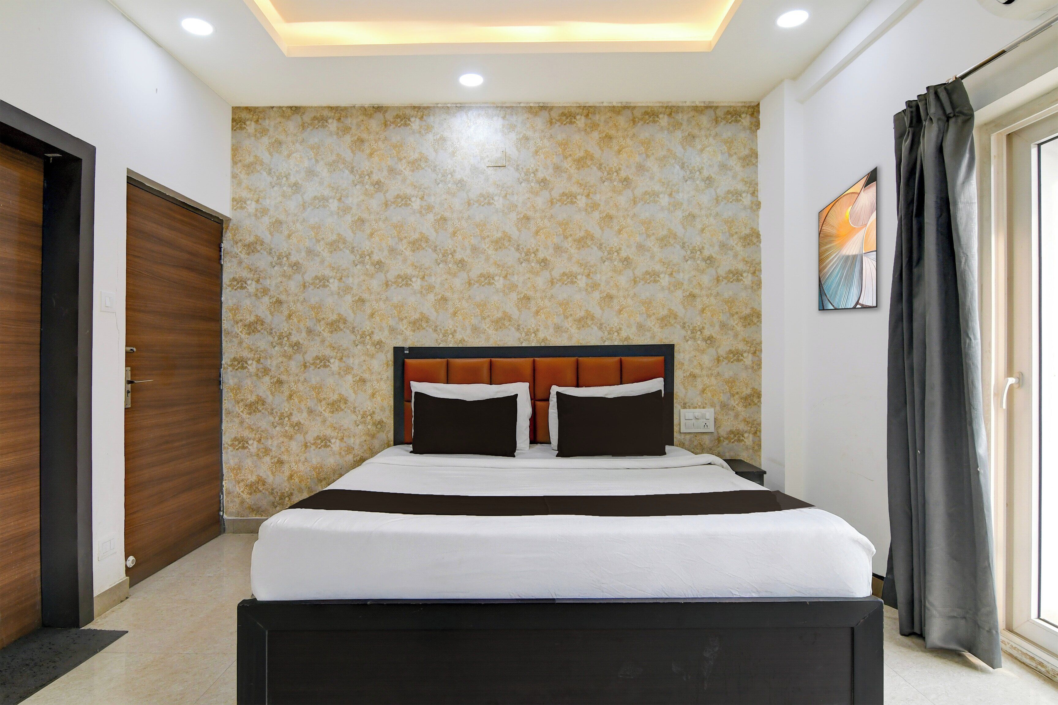Un dormitorio con cama, cabecera, pared con estampado floral, puerta y ventana con cortinas.