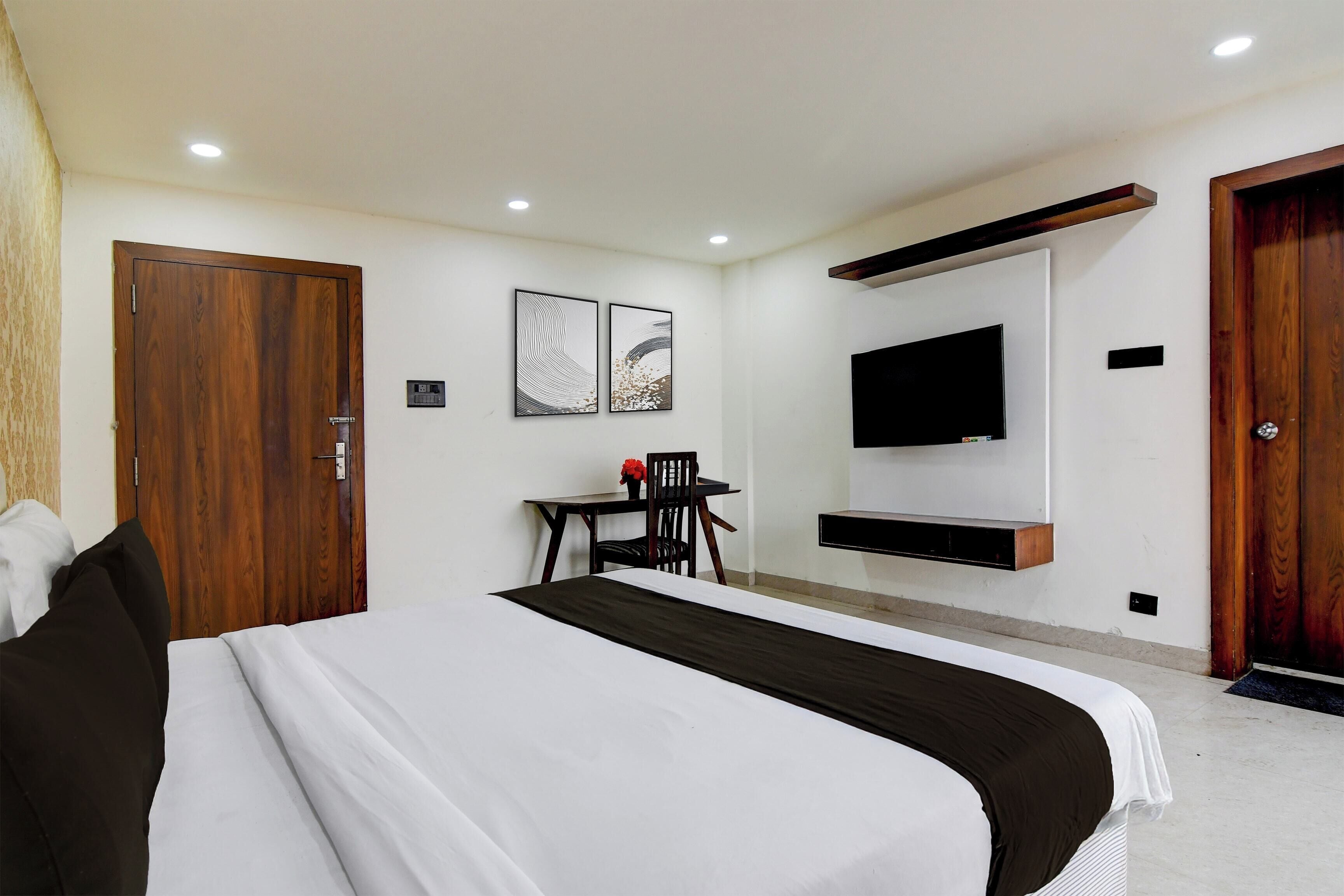 A hotel room with a large bed, a desk with a chair, a flat-screen TV mounted on the wall, and wooden doors.