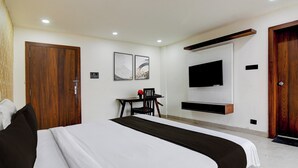 A hotel room with a large bed, a desk with a chair, a flat-screen TV mounted on the wall, and wooden doors. - Collection O Infocity Square Bhubaneswar (Bhubaneshwar)