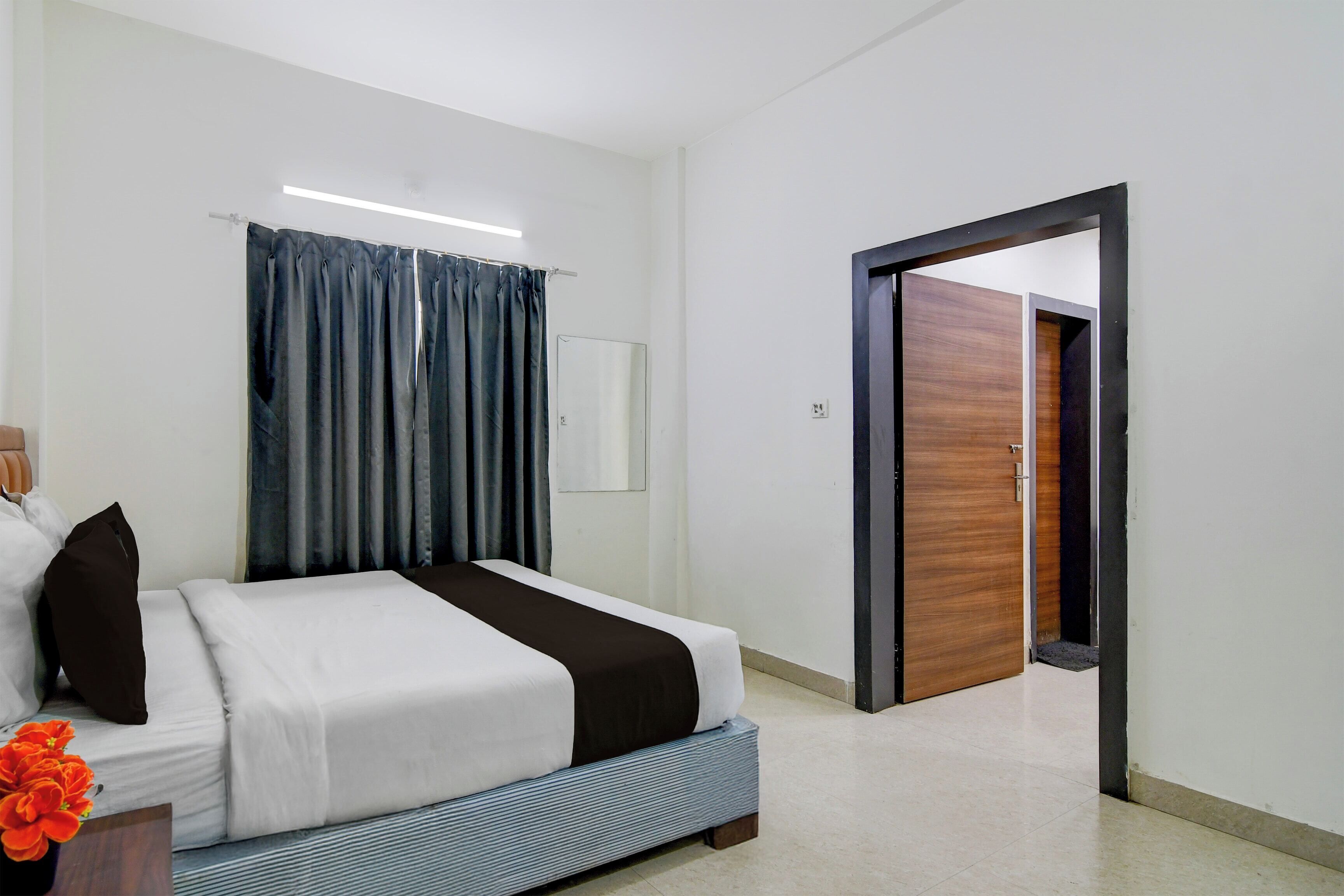 Una habitación de hotel con cama, espejo, puerta y ventana con cortinas.