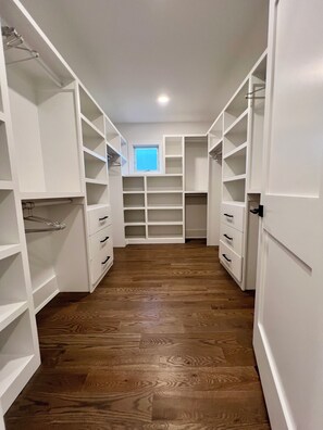 Ein begehbarer Kleiderschrank mit offenen Regalen, Schubladen und einem Fenster am Ende.