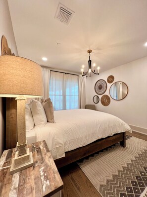 A bedroom with a large bed, a wooden nightstand, a chandelier, and decorative wall mirrors. - Spacious 4-bedroom house in peaceful Long Branch with AC (Long Branch)