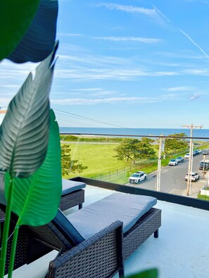 A balcony with wicker furniture overlooking a parking area and a view of the sea. - Spacious 4-bedroom house in peaceful Long Branch with AC (Long Branch)