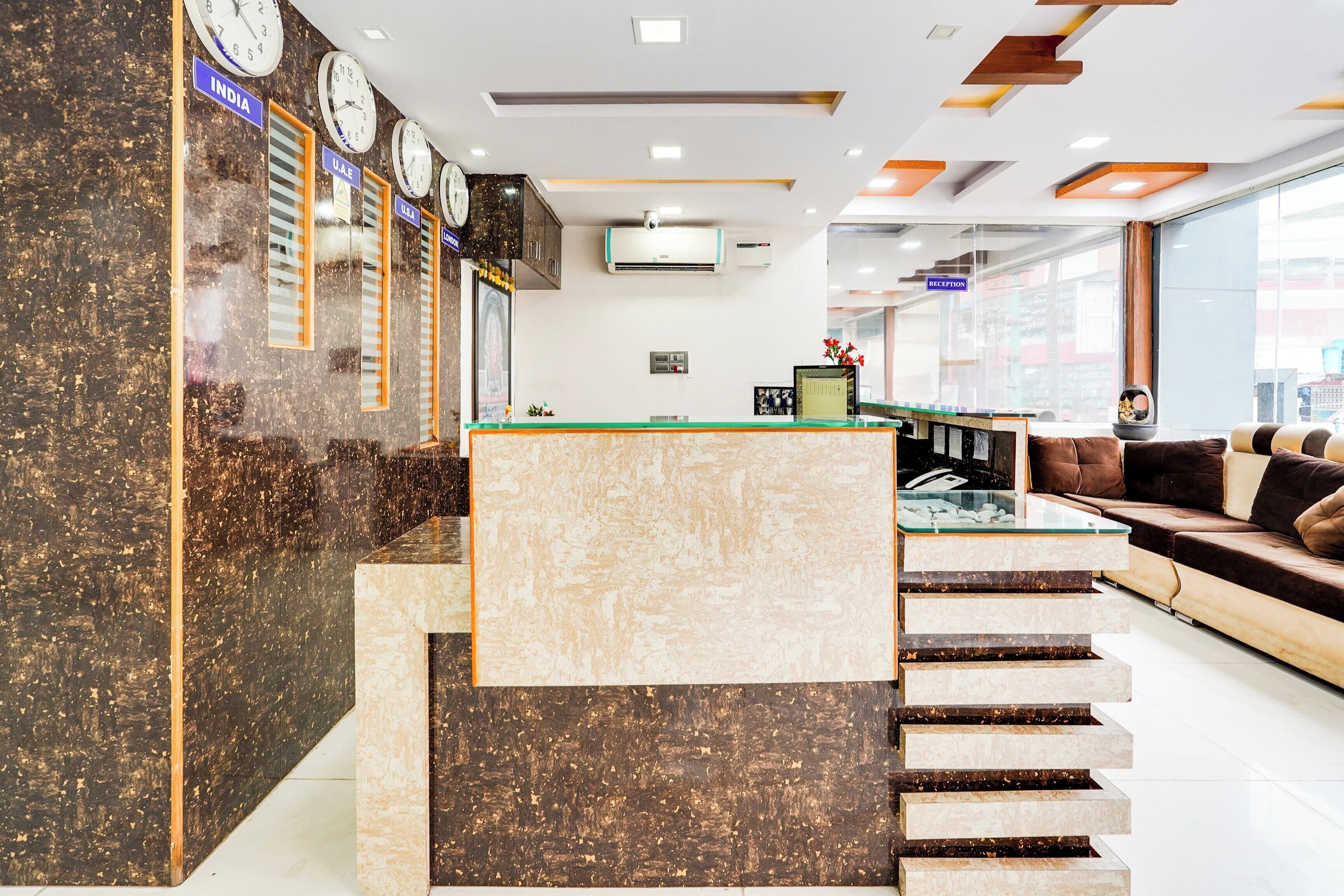 A hotel lobby with a reception desk, clocks, a staircase, and seating area.