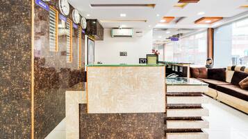 A hotel lobby with a reception desk, clocks, a staircase, and seating area.