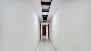 Un long couloir étroit aux murs blancs et au sol carrelé, qui mène à une porte au fond.
