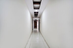 Un long couloir étroit aux murs blancs et au sol carrelé, qui mène à une porte au fond.